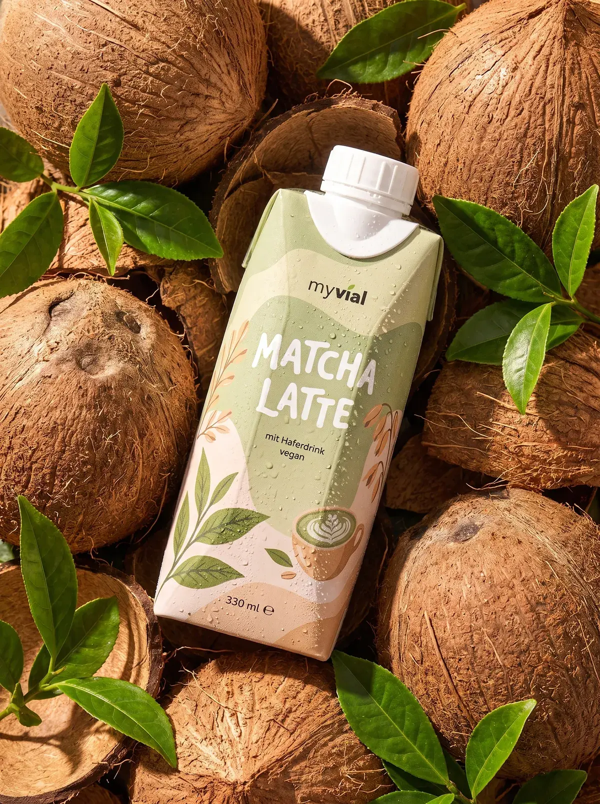 Packung myvial Matcha Latte zwischen Kokosnüssen und frischen Teeblättern