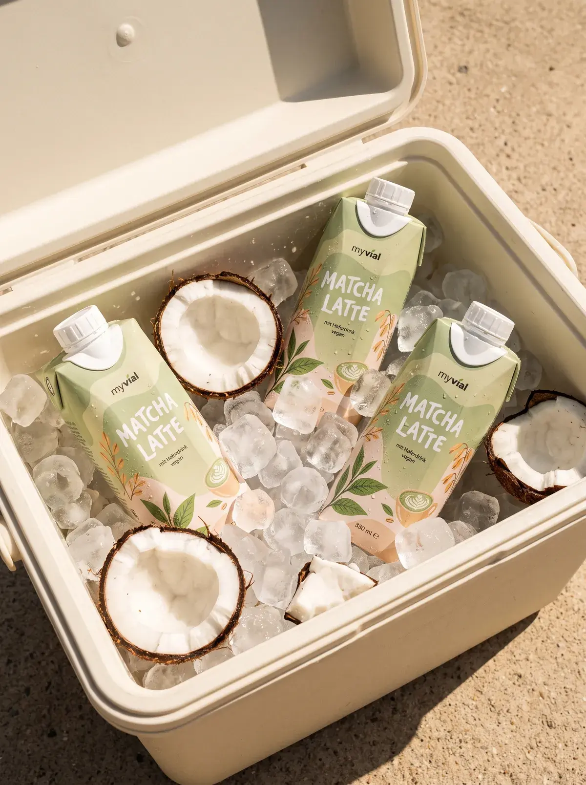 Kühlbox mit Eis, drei Packungen myvial Matcha Latte und aufgeschlagenen Kokosnüssen