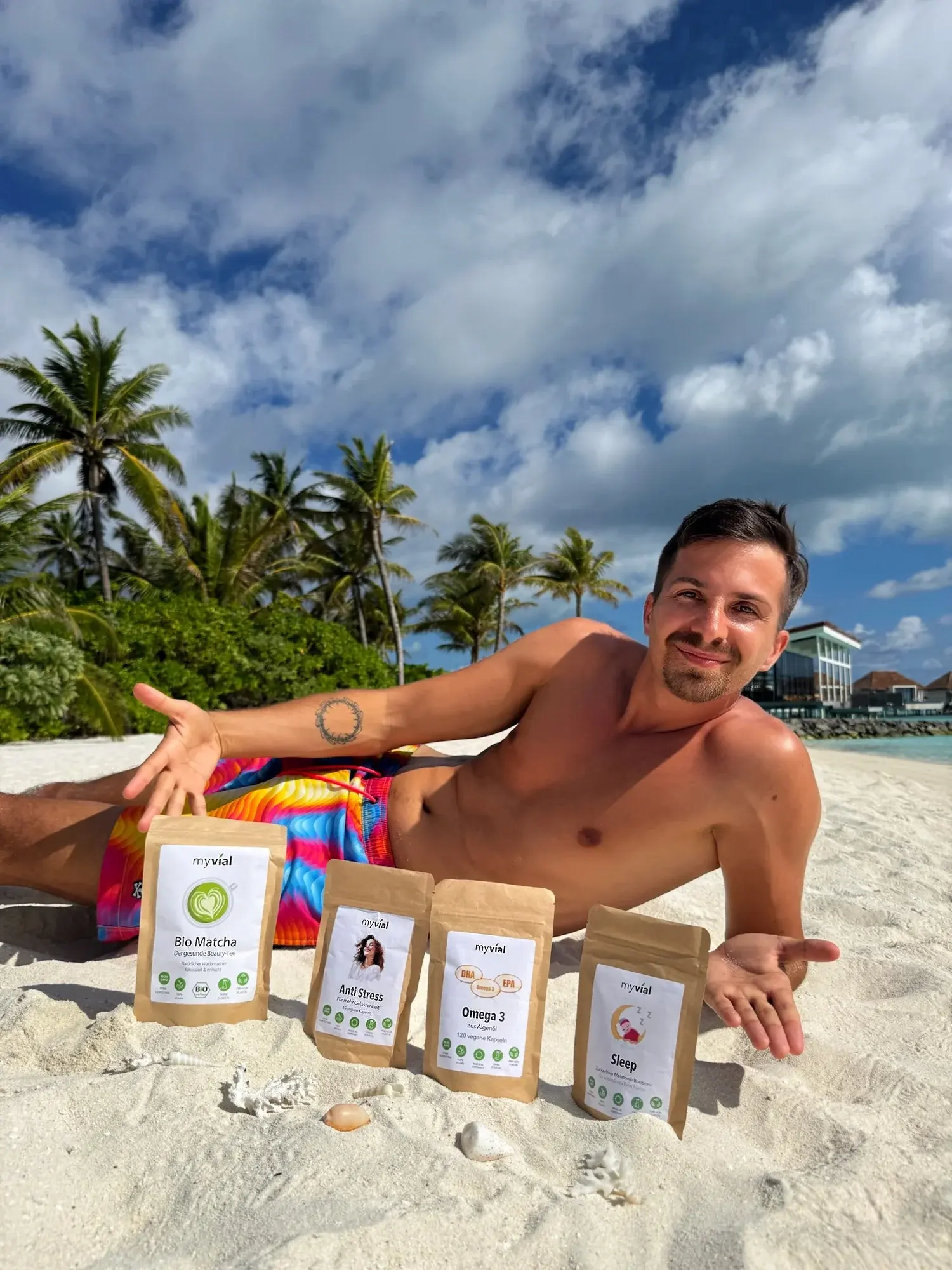 Michael liegt am Strand neben vier myvial-Produkten in Papierbeuteln